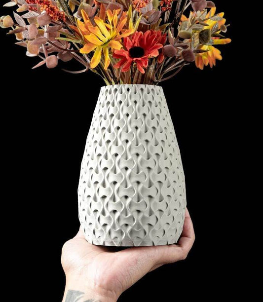 Hand holding eco-friendly 3D printed white bioplastic vase with sculptural texture and dried flowers against black background