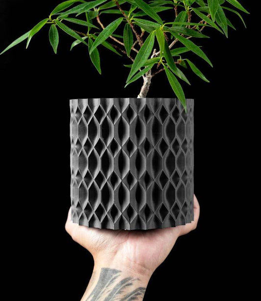 Eco-friendly 3D printed planter with geometric texture held in hand containing a small leafy plant